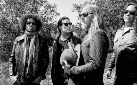 Medlemmar av Alice in Chains, fyra män med solglasögon, står utomhus bland träd. En håller en hatt med fjädrar.