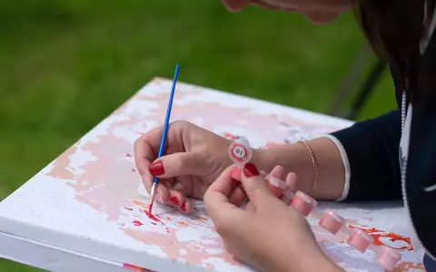Kobieta maluje obraz po numerach, trzymając pędzel i małe pojemniczki z farbą. Uczy się, jak namalować coś ładnego.