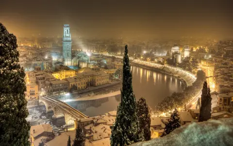 Verona innevata, un'incantevole **città da visitare a dicembre**. La neve copre i tetti e il fiume Adige riflette le luci della città.