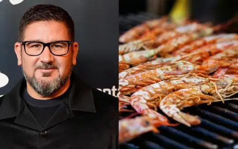Hombre con gafas y barba junto a una parrilla llena de cigalas a la plancha, listas para ser degustadas.