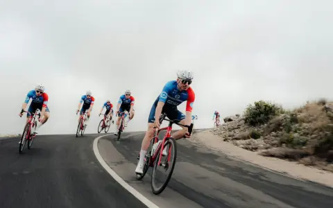 Cyclists in blue and red kits race downhill, showcasing the intense effort behind the Tour de France average speed.
