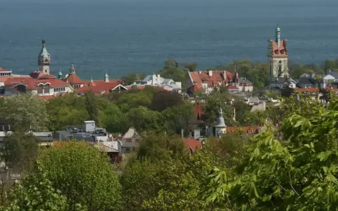 Widok na miasto z wieżą widokową w Kolibkach, otoczone zielenią drzew, z morzem w tle.