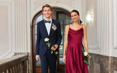 Elegantes Outfit für einen Jugendweihe Gast: Ein junger Mann im dunkelblauen Anzug mit Fliege und eine Frau im weinroten Kleid.