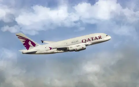 Qatar Airways Airbus A380 airplane in flight against a cloudy blue sky.