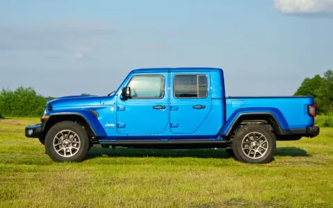 Niebieski Jeep Gladiator na tle zielonej łąki i drzew. Ten wszechstronny pickup jest gotowy na każdą przygodę.