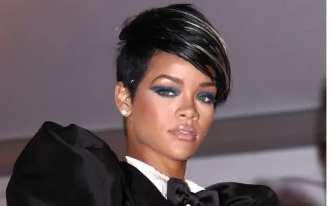 Une femme arbore une coupe femme carré rasé coté, avec un maquillage audacieux et une tenue élégante.