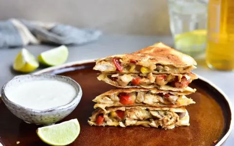 Stos **quesadilli z kurczakiem**, papryką i serem, podane z dipem i limonką.