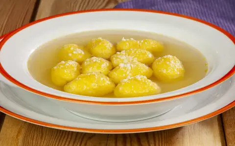 Una ciotola di semolino dosi per 1 persona, con palline dorate in brodo, cosparse di formaggio grattugiato.