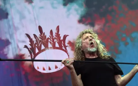 Wokalista Led Zeppelin, Robert Plant, śpiewa z pasją na tle scenografii z koroną.