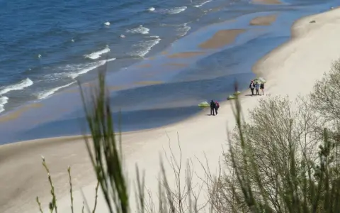Plaża z falami, piaskiem i kilkoma spacerującymi osobami, widok z klifu.