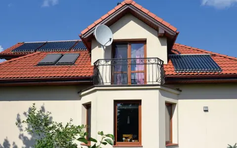 Elegancki wykusz w domu z balkonem i anteną satelitarną. Na dachu widoczne kolektory słoneczne.