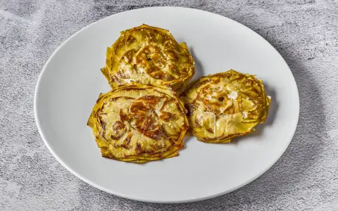 Tres alcachofas cortadas en rodajas, cocinadas a baja temperatura, con un toque de sal marina, servidas en un plato blanco.