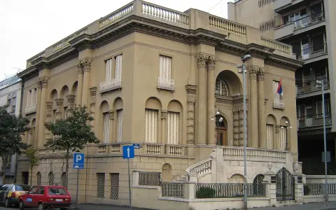 Elegancki budynek, Muzeum Tesli, z kolumnami i łukami. Przed nim schody i ogrodzenie.