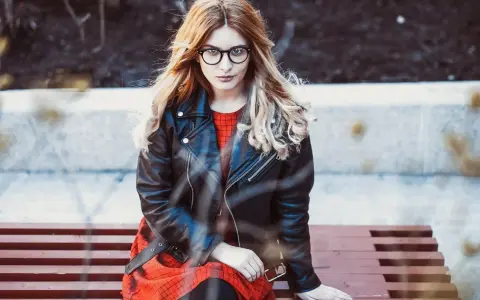 Dziewczyna w okularach i czerwonej sukience siedzi na ławce, ubrana w stylową kurtkę Dolce & Gabbana.