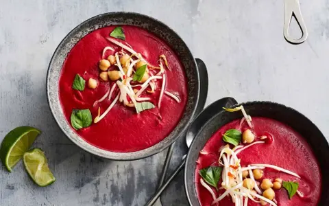 Zwei Schalen cremiger, **roter Bete Suppe mit Kokosmilch und Orangensaft**, garniert mit Kichererbsen und Sprossen.