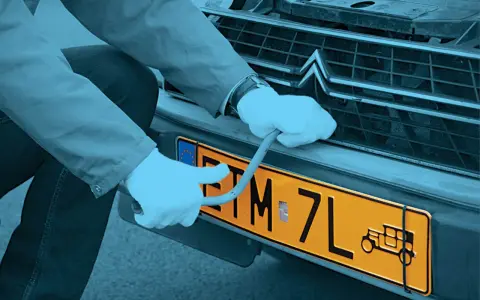 Ręce w białych rękawiczkach montują żółtą tablicę rejestracyjną z symbolem starego auta. Czy warto zarejestrować auto jako zabytek?