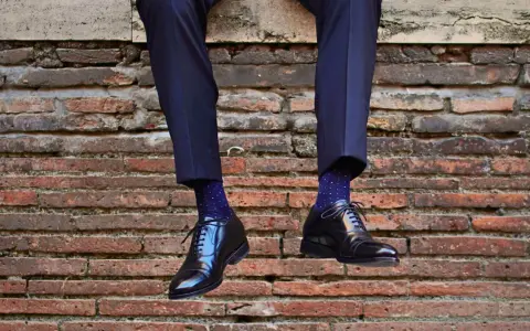 Uomo con calzini blu a pois bianchi e scarpe nere lucide. Un perfetto abbinamento calzini scarpe uomo per un look elegante.