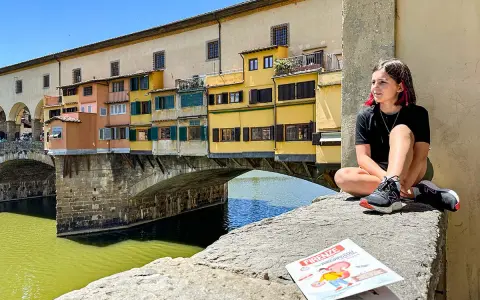 Ragazza seduta sul Ponte Vecchio, con la guida "Firenze cosa vedere in due giorni" a fianco.