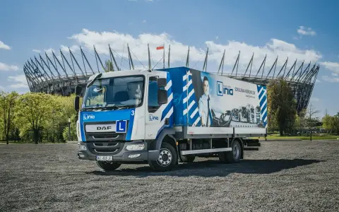 Ciężarówka szkoleniowa z literą "L" na masce, gotowa do nauki jazdy kat. C. W tle stadion.
