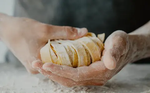 Dłonie trzymają świeży, pokrojony makaron. Zastanawiasz się, ile makaronu na porcję?