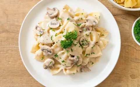 Szybki obiad z makaronem farfalle w kremowym sosie grzybowym, posypany natką pietruszki. Idealny na szybki posiłek.