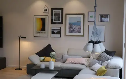 Przytulne mieszkania w Danii: salon z wygodną kanapą, galerią ścienną i designerską lampą.