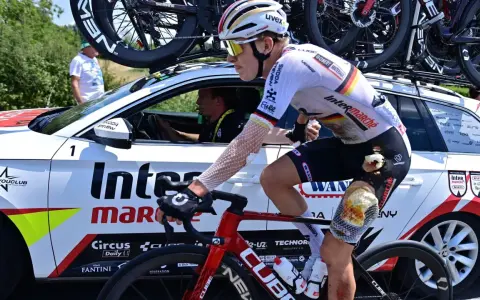 Radfahrer Georg Zimmermann mit aufgeschürftem Knie fährt neben dem Begleitfahrzeug des Teams Intermarché-Wanty.