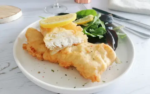 Poisson pané croustillant, servi avec une salade verte et des quartiers de citron. Un délice de fish and chips !
