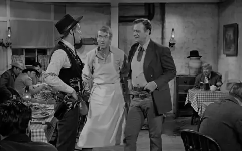 Inquadratura americana di tre uomini in un saloon. Uno indossa un grembiule, gli altri abiti western.