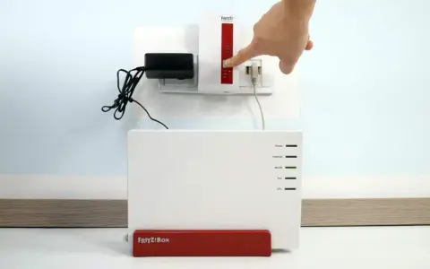 Finger drückt Knopf am Fritz!Repeater, um das **wifi repeater einrichten** zu starten. Fritz!Box steht daneben.