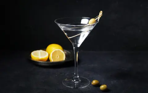 En klassisk vodka martini med en oliv på en tandpetare. Citroner ligger på en tallrik i bakgrunden.
