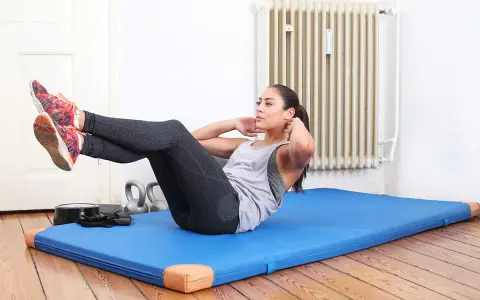 Frau macht Crunches auf einer blauen Matte. Sie trainiert ihren Bauchmuskel, um fit zu bleiben.