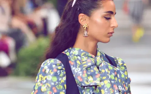 Ein dezenter Haarkamm hält die elegante Frisur einer Frau mit auffälligem Ohrring und geblümtem Kleid im Zaum.