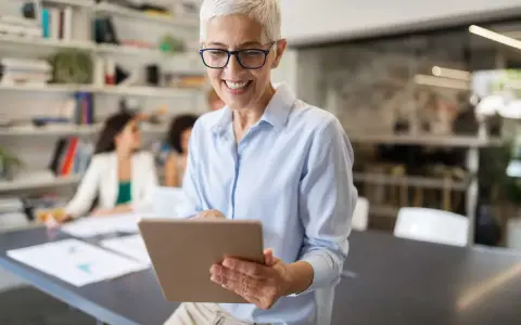 A smiling woman reviews a board chair job description on a tablet in a modern office.