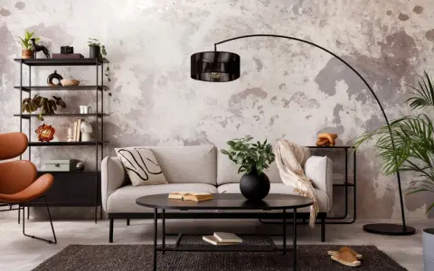 Sofá gris, mesa negra y estantería metálica en una sala con decoración estilo industrial chic. Pared texturizada y silla naranja.