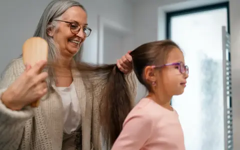Babcia czesze wnuczkę, a jej siwe włosy przypominają o tym, dlaczego wypadają włosy.