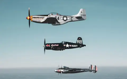Drei historische Flugzeuge im Flug: eine silberne P-51 Mustang, ein schwarzer Red Bull Flieger (Corsair) und eine P-38 Lightning.