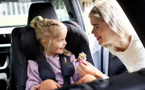 Uśmiechnięta mama daje córeczce w foteliku samochodowym bukiecik kwiatów. To miły test plus dla małej pasażerki.