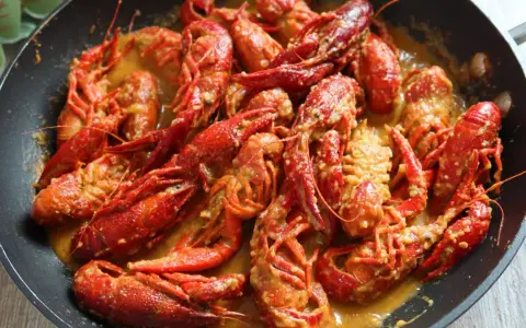 Un delicioso cangrejo de río en una sartén, bañado en una cremosa salsa. ¡Un manjar listo para disfrutar!