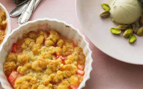 Rhabarber-Crumble in weißer Auflaufform, daneben eine Kugel Eis mit Pistazien. Ein köstliches Rhabarber Dessert.
