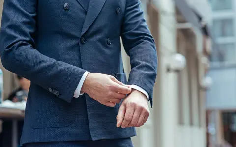 Uomo che sistema il polsino della sua giacca blu, un perfetto abbinamento giacca blu uomo per un look elegante.
