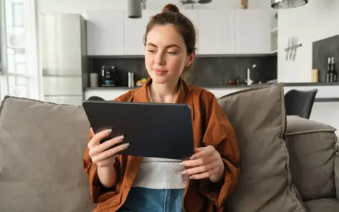 Kobieta na kanapie przegląda tablet, być może szukając informacji o kursach fakultatywnych.