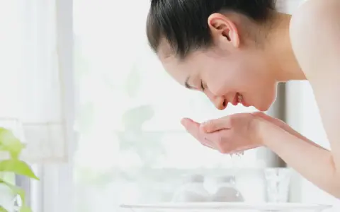 Eine Frau wäscht ihr Gesicht mit Seife und Wasser. Sie hält ihre Hände schöpfend unter fließendes Wasser, um ihr Gesicht zu reinigen.