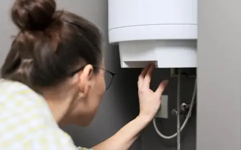Une femme vérifie le réglage de son chauffe-eau. Peut-on laisser un chauffe-eau en marche forcée ? La réponse dépend de votre appareil.