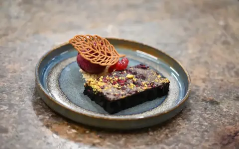 Elegancki deser: monoporcja brownie z malinami i lodami, ozdobiona listkiem z ciasta. Kontrastuje z tradycyjnymi blachami ciasta.