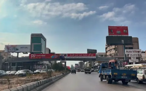 Driving in Lebanon, a busy street with cars, trucks, and billboards advertising various services and products.