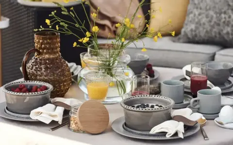 Vacker dukning runt bordet med frukostskålar, bär, juice och en vas med gula blommor.