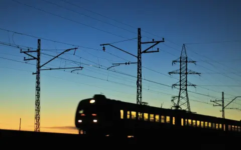Pociąg w ruchu na tle zachodzącego słońca i linii energetycznych.