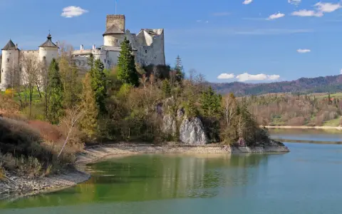 Majestatyczne zamki Małopolska na wzgórzu nad jeziorem, otoczone zielenią i górami.