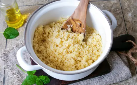Ein Topf mit frisch gekochtem Couscous, bereit für ein einfaches Couscous-Rezept. Ein Holzlöffel rührt die Körner auf.